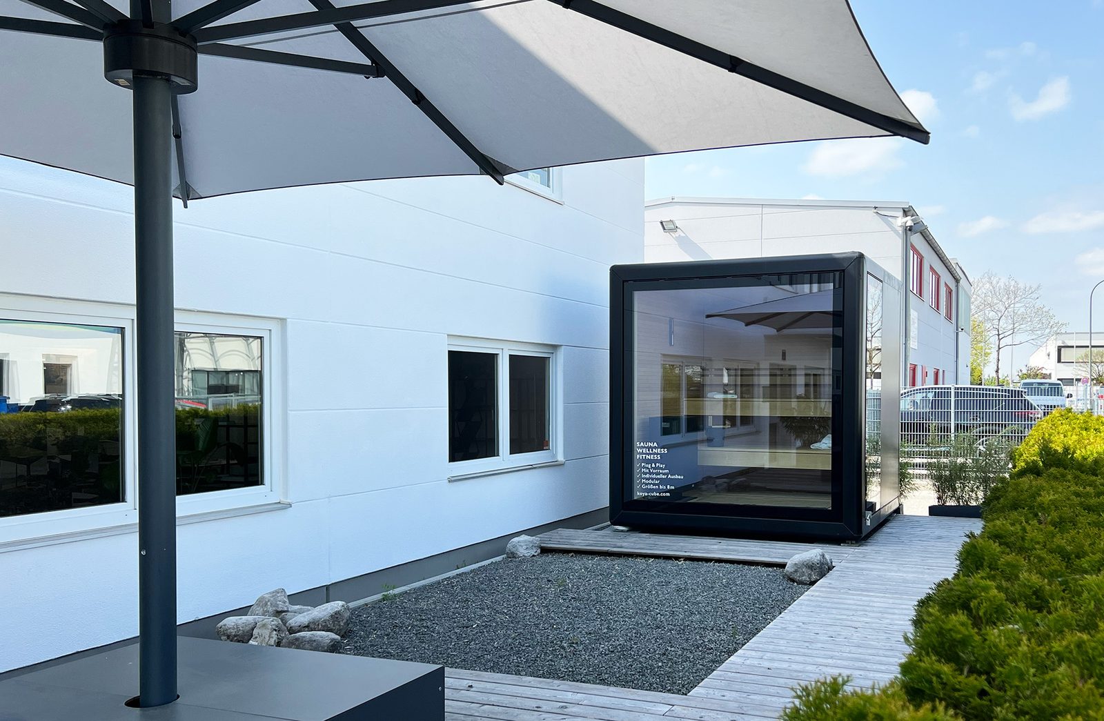 Aufnahme: Schwarzer KOYA Sauna Cube mit Glasfront im Garten neben einem Wohnhaus, Thema Genehmigung der Sauna im Garten