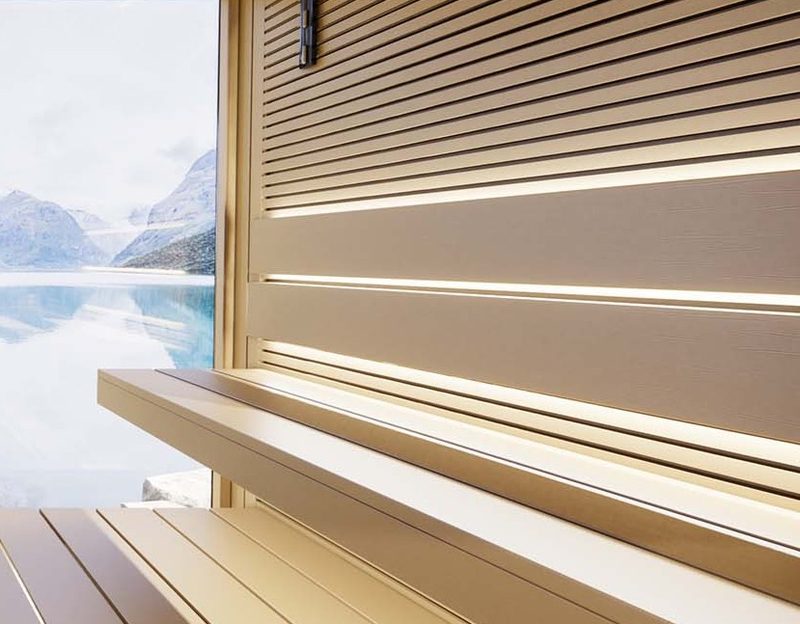 Warmweiße Lichtfugen zwischen den Brettern der Rückenlehne über der Saunabank, links Fenster zum Bergsee