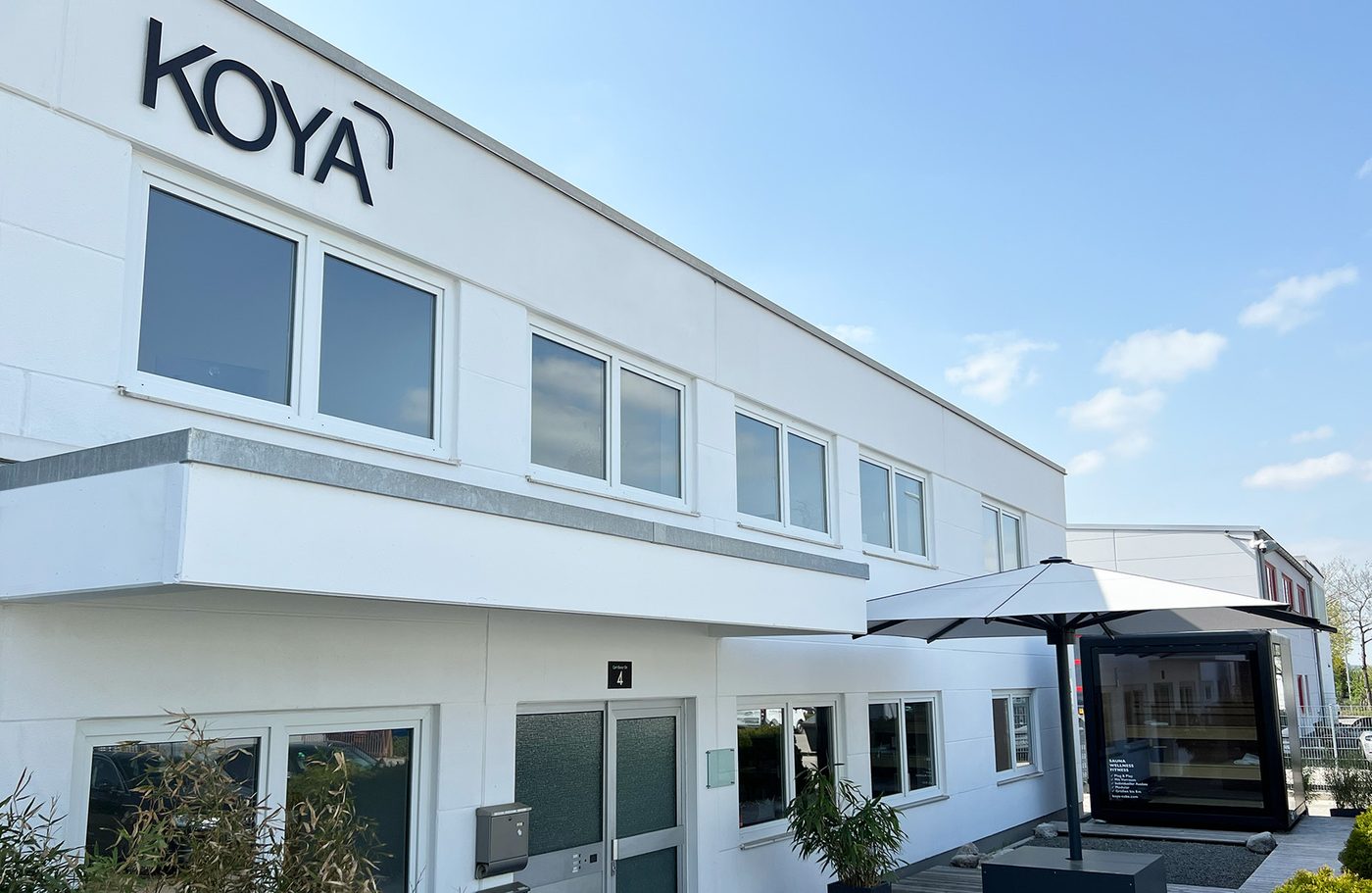 Firmengebäude von KOYA in Gilching mit Schriftzug, davor ein schwarzes Modul mit Glasfront