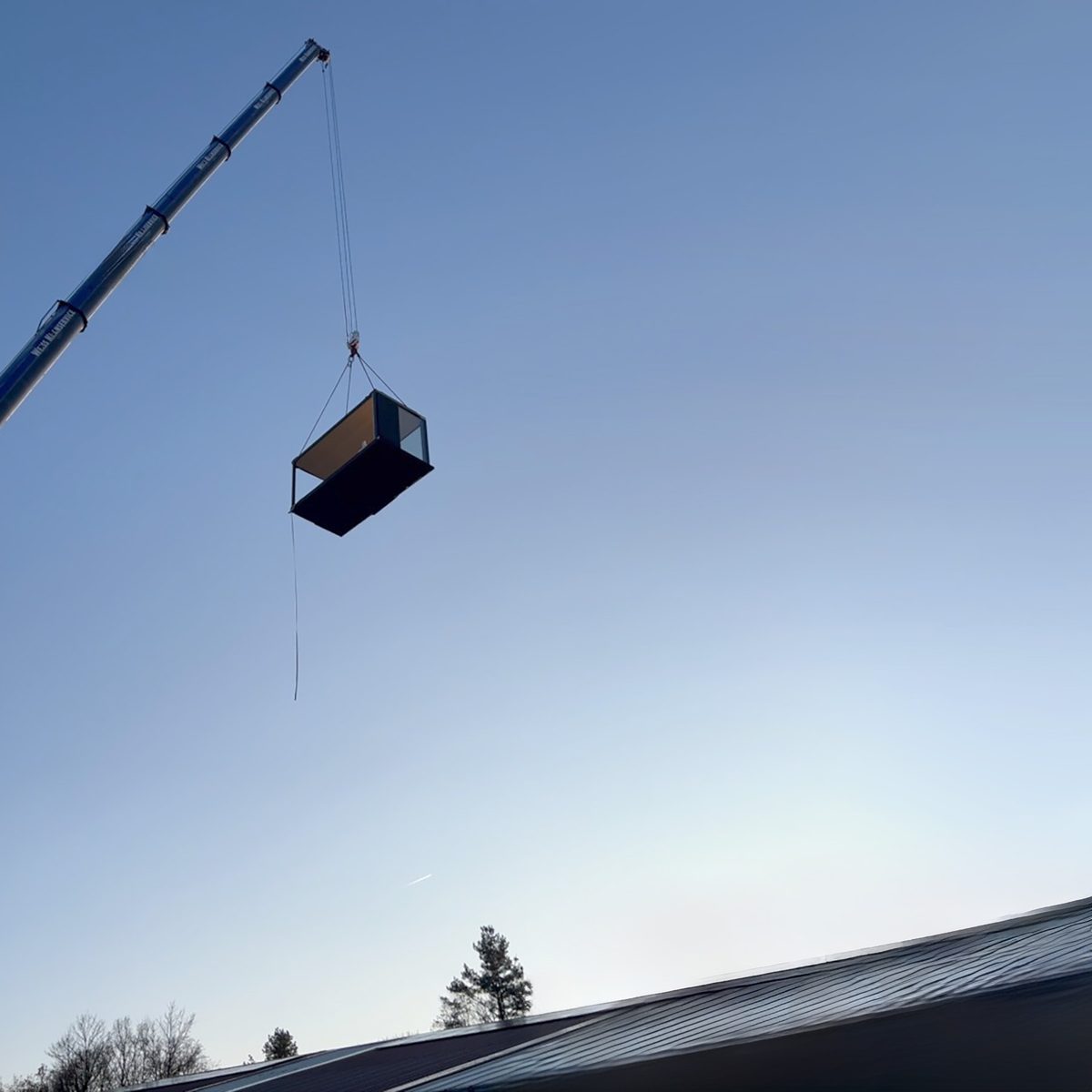 Ein KOYA Verkaufspavillon schwebt am Haken eines Autokrans vor blauem Himmel