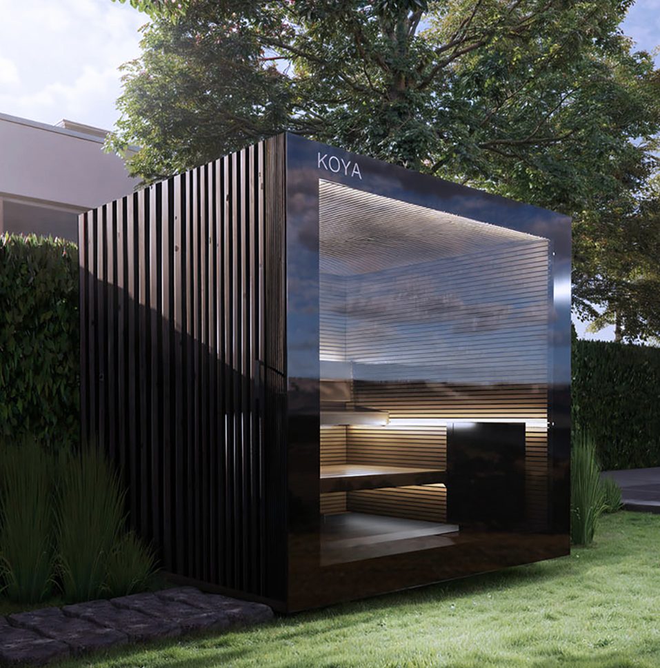 Sauna mit schwarz spiegelnder Glasfront, KOYA-Schriftzug und senkrechten Lamellen im Garten vor einer Hecke