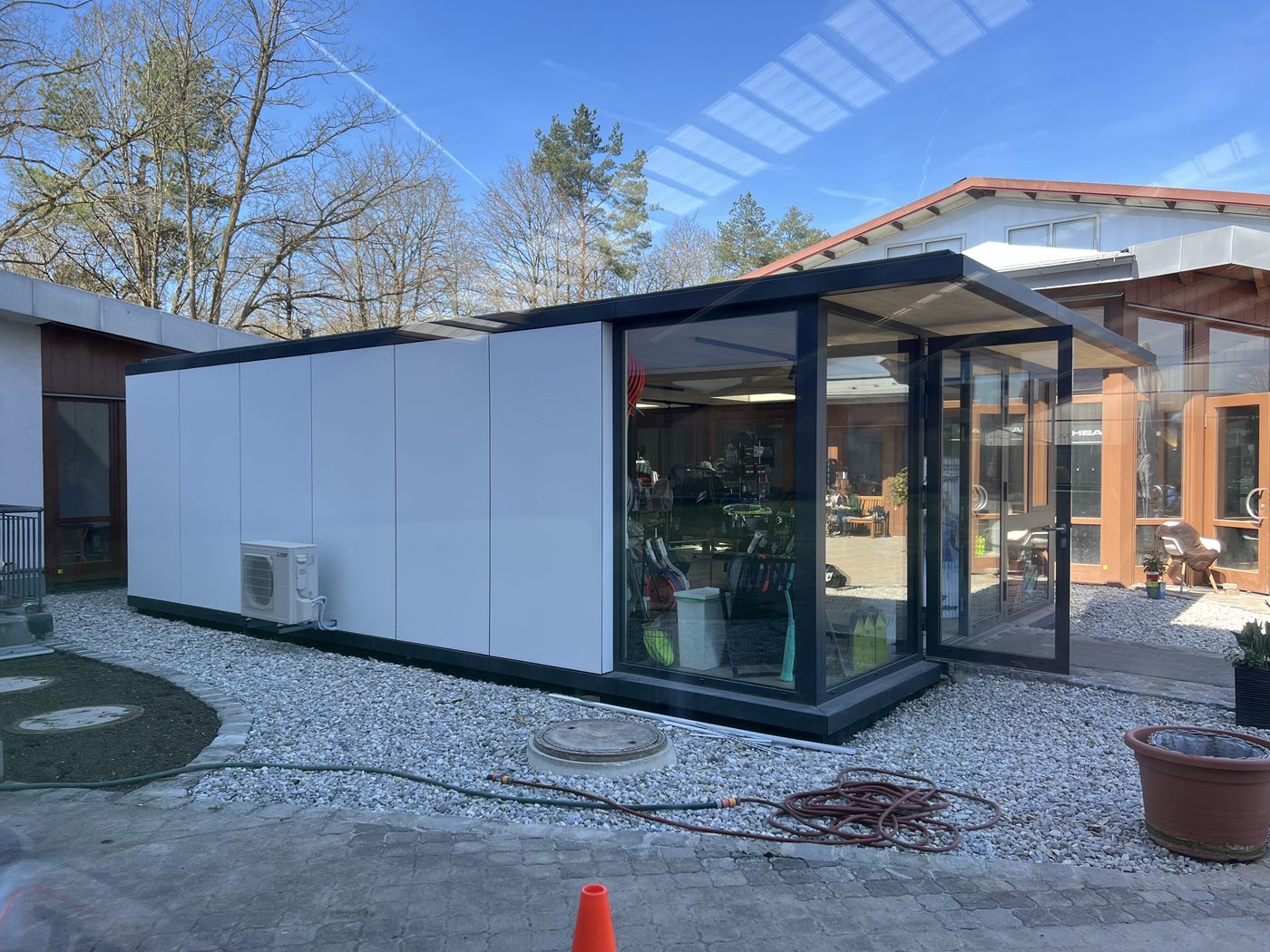 Modulbau mit weißen Fassadenplatten und verglastem Eingang auf Kies in Taufkirchen, innen Tennisschläger
